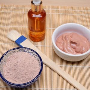 A bowl of clay next to some brush and a bottle.