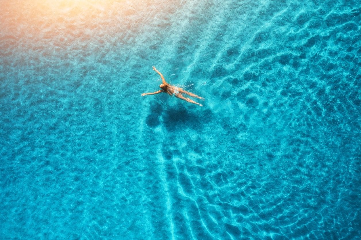 An eco-friendly aerial view of a woman floating in the blue water.