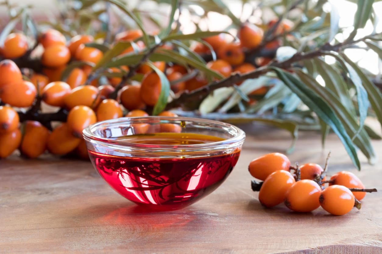 A bowl of liquid with orange berries on a wooden table.