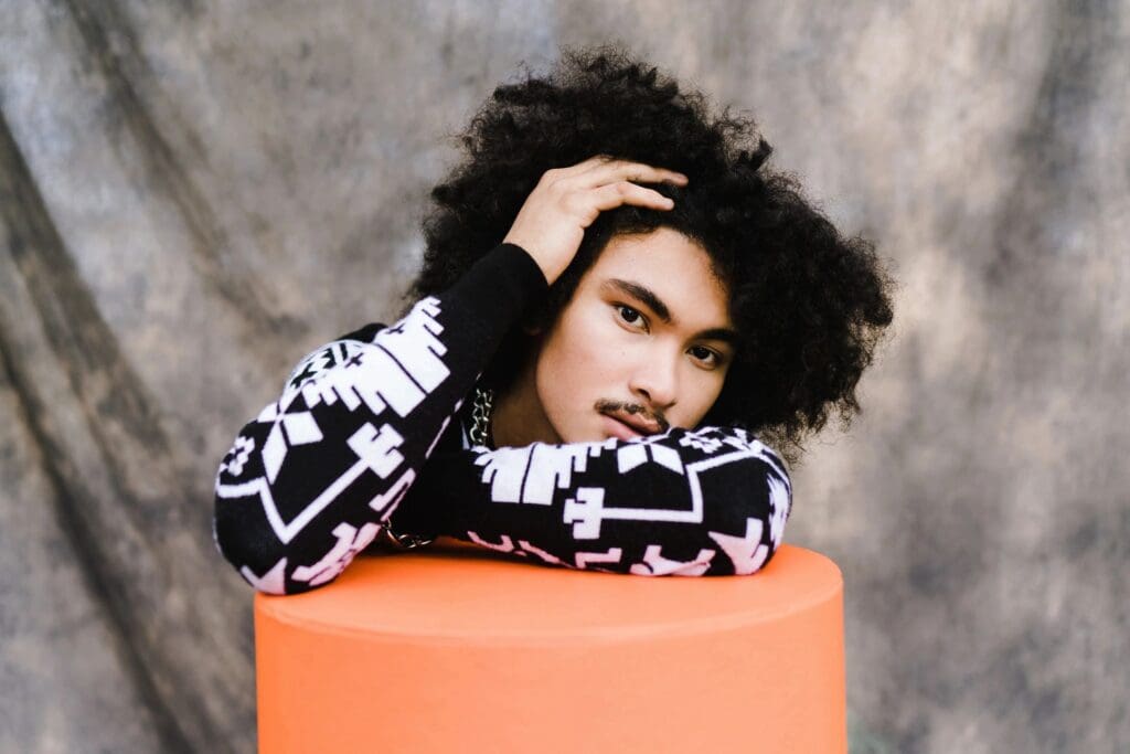 A person with curly hair sitting on top of a orange cylinder.