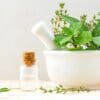 A mortar and pestle with herbs in it next to a bottle of essential oil.