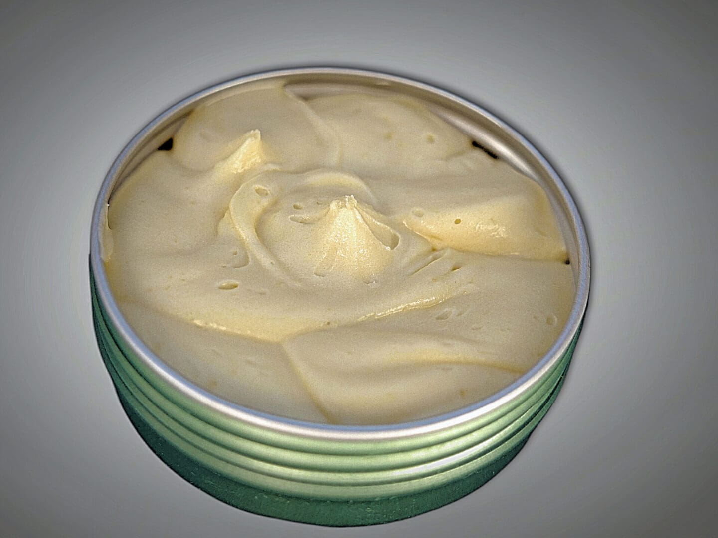 A tin of whipped cream on a grey background, resembling Nature's First Aid Body Butter.