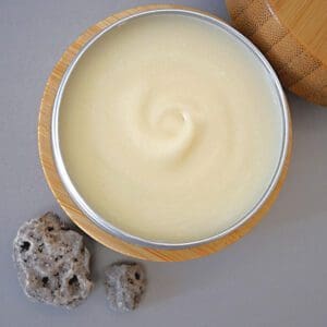 A tin of natural body butter on a table next to a rock.