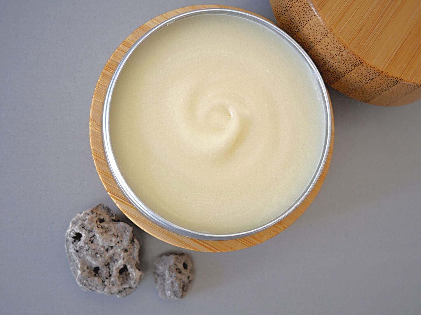 A tin of natural body butter on a table next to a rock.