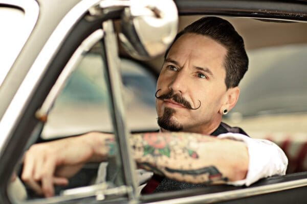 A man with a mustache sitting in the drivers seat of a car.