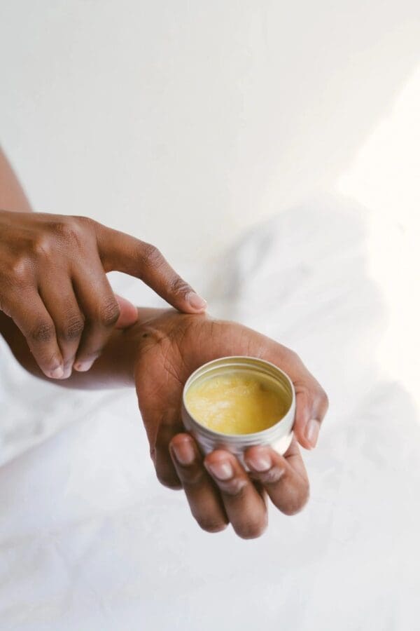 A person holding an open hand with a jar of cream.