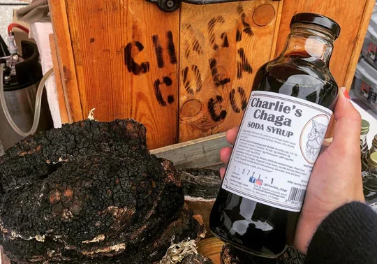 A person is holding a bottle of black licorice in front of a crate.