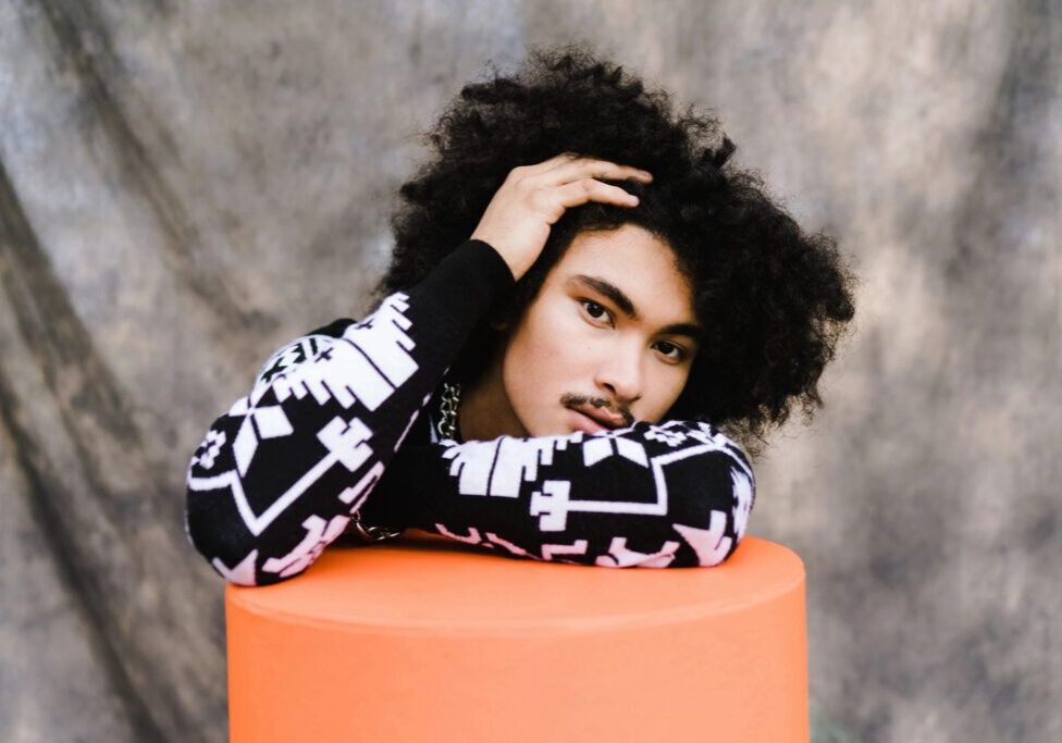 A person with curly hair sitting on top of a orange cylinder.