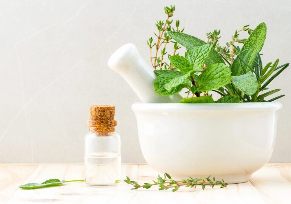 A mortar with herbs and a bottle of essential oil on a wooden table.